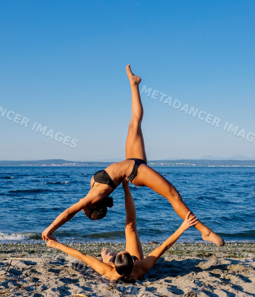 Two women doing partner acrobatics yoga on a beach in wa USA