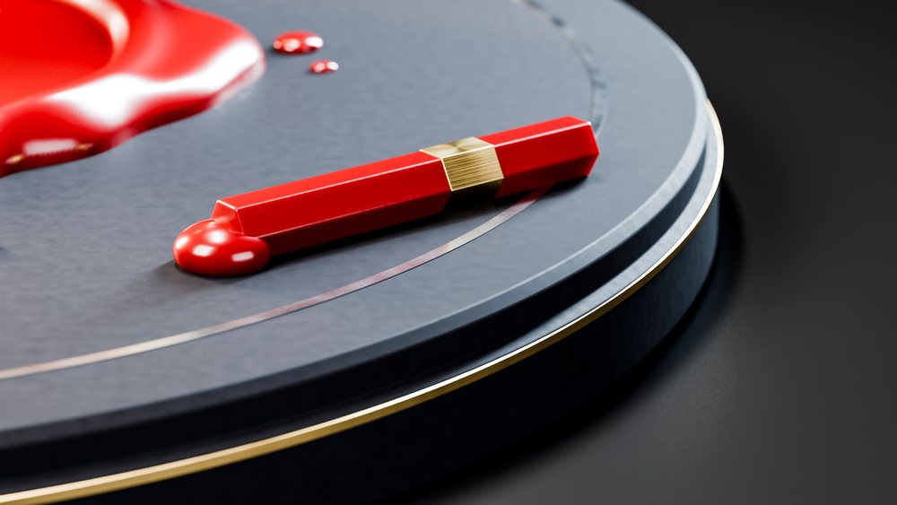 Red lipstick tube with gold band resting on a glossy black circular surface in a modern setting.