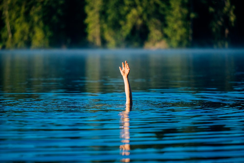Hand raised above calm lake water with a forest and morning mist in the background, USA.