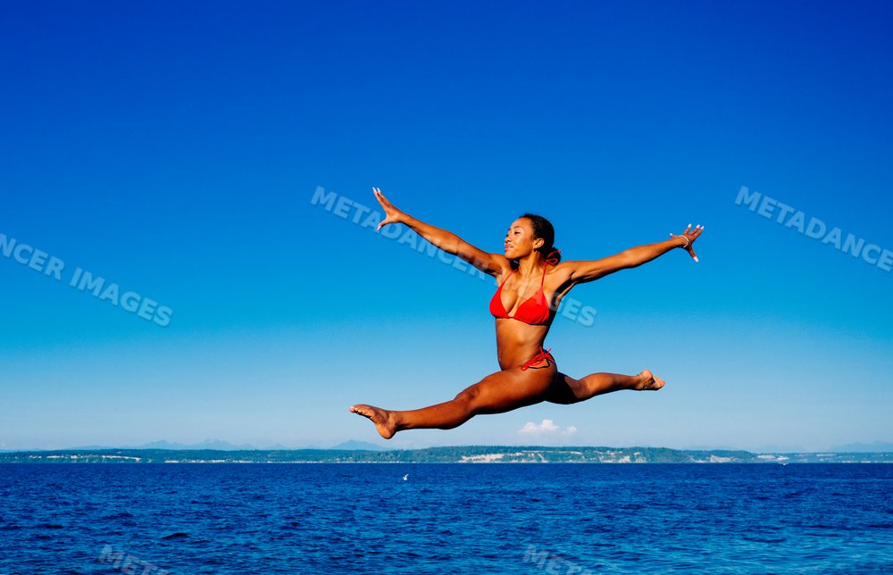 A woman in swimwear jumps over the ocean on a clear day in WA, USA