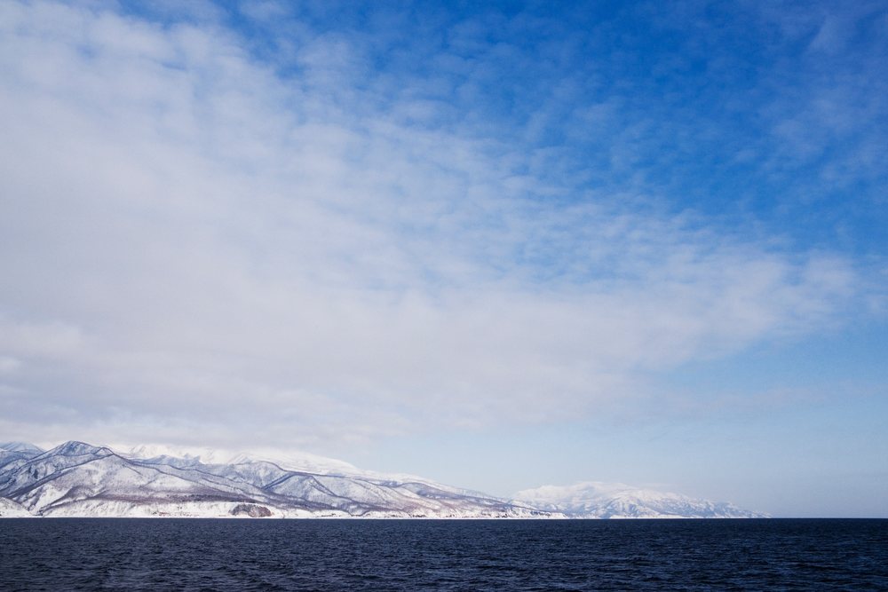 Snow-covered mountains along Nemuro Channel at Shiretoko Peninsula, Hokkaido, Japan under a partly cloudy winter sky, Asia.