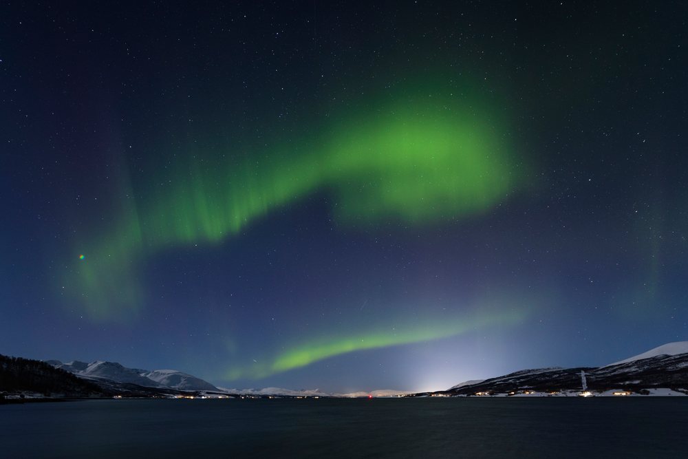 Northern Lights illuminate the clear night sky over snowy mountains and calm waters at Balsfjorden, Landscape, Mestervik, Norway.