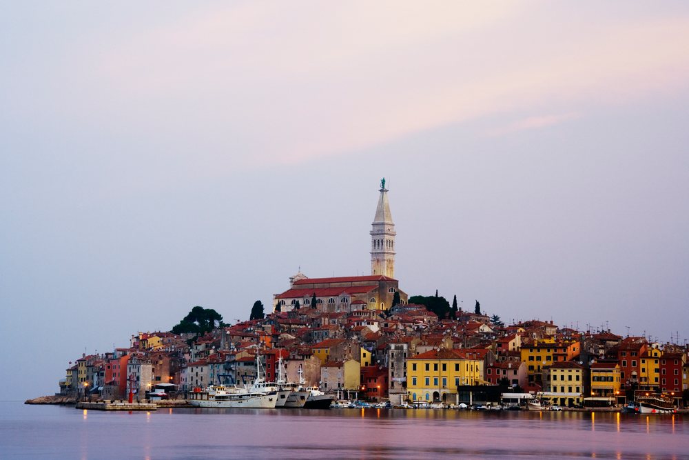 Dawn over the town of Rovinj shows boats moored in the harbor with a church tower rising above buildings, Croatia.