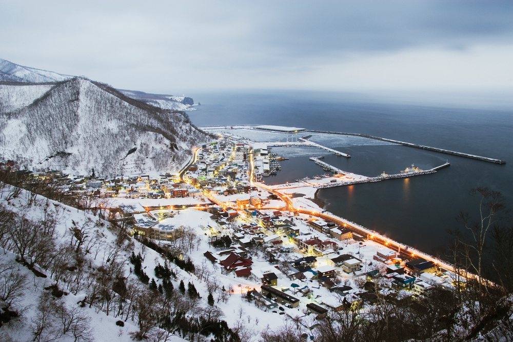 Rausu town lights glow on a snowy winter coast beside the sea on Shiretoko Peninsula, Japan, Asia.