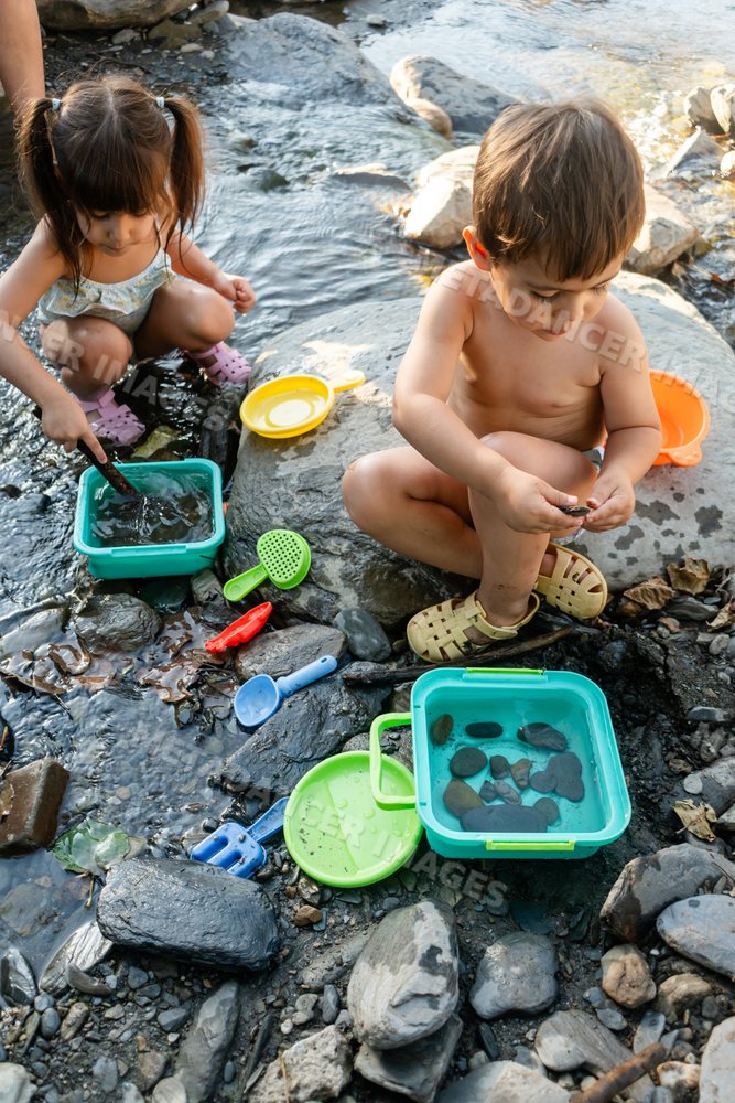 Two white children playing with water and rocks outdoors by a stream