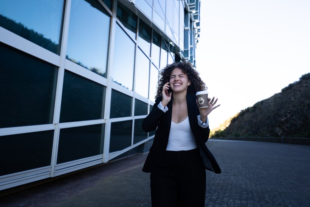Professional woman smiling while talking on the phone and holding a coffee cup outside a modern building, businesswoman, business trip, Spain, Santiago De Compostela.