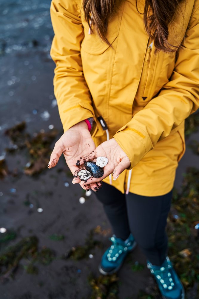 White Woman holding shells with muddy hands on a beach in a beach