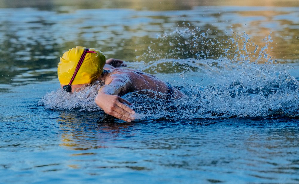 Swimmer wearing a yellow swim cap performing freestyle stroke in open water with splashing water, USA.