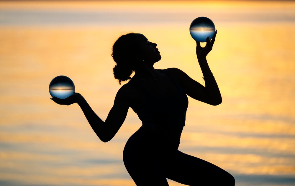 Woman balancing two crystal balls while posing at sunset outdoors, yoga, acrobatics, USA.