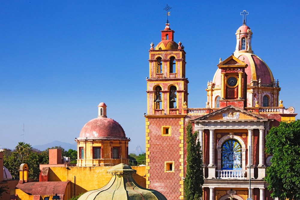 Santa Maria de la Asuncion church features a bell tower and red domes under a clear blue sky, Queretaro, Mexico.