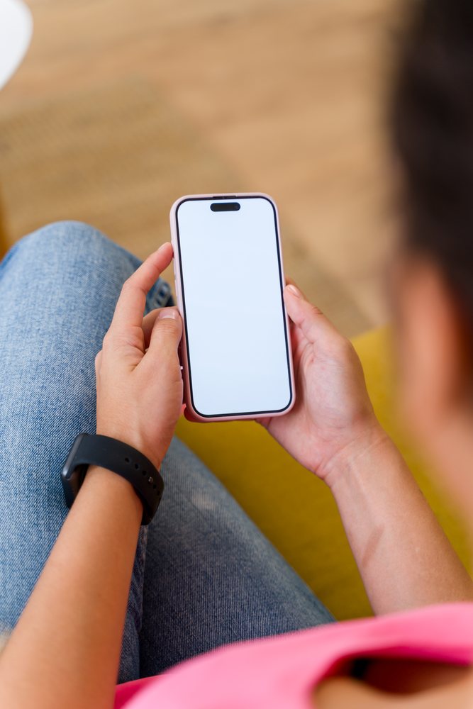 A person holding a smartphone with a blank screen while sitting indoors in a casual setting, Spain.