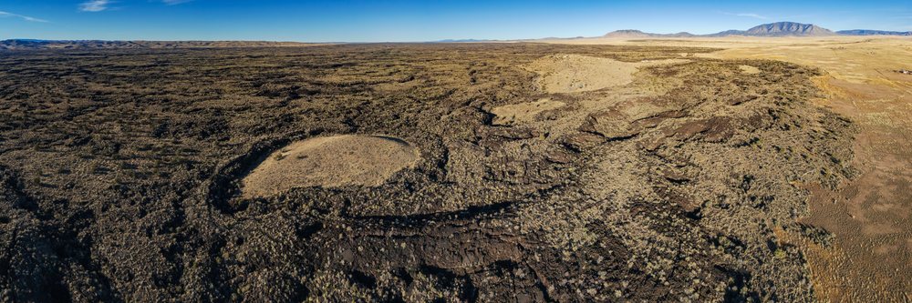 Aerial view shows volcanic lava fields and rocky terrain with dry vegetation at El Malpais National Monument, New Mexico under a clear sky, landscape, wildlife, Carrizozo, USA.