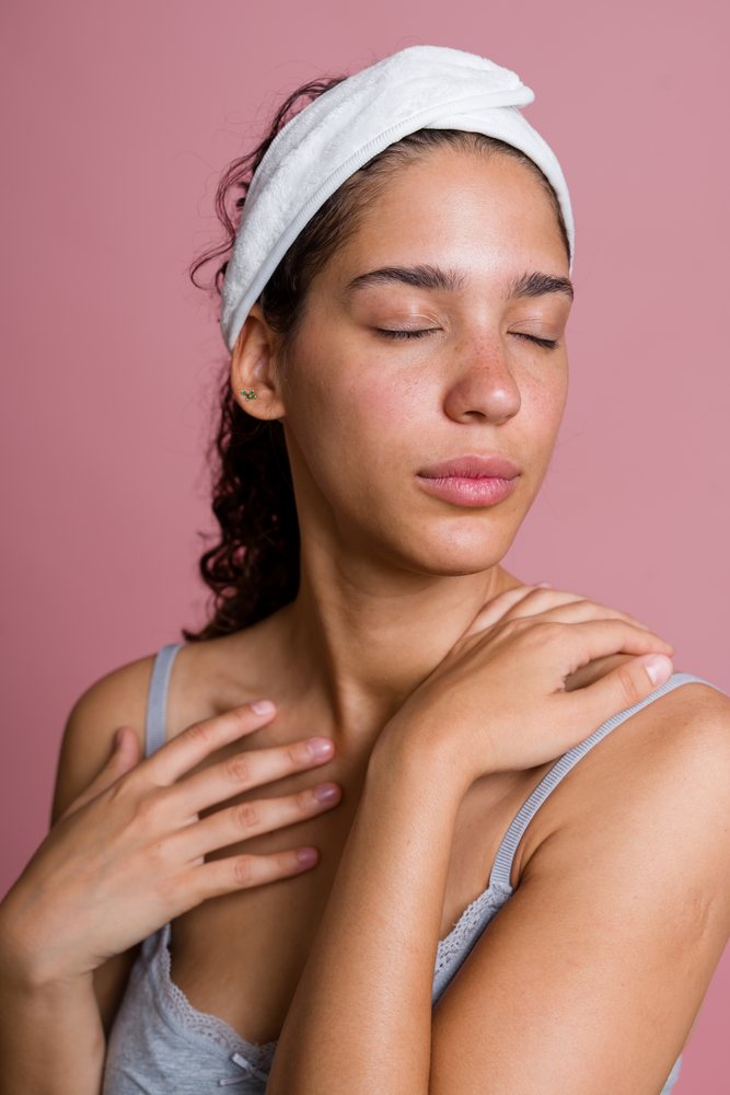 Woman with closed eyes wearing a white headband touching her shoulder against a pink background in a beauty shoot, Spain.