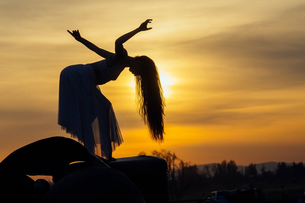Woman performing a graceful dance silhouette at sunset outdoors in the USA, her long hair flowing and dress.
