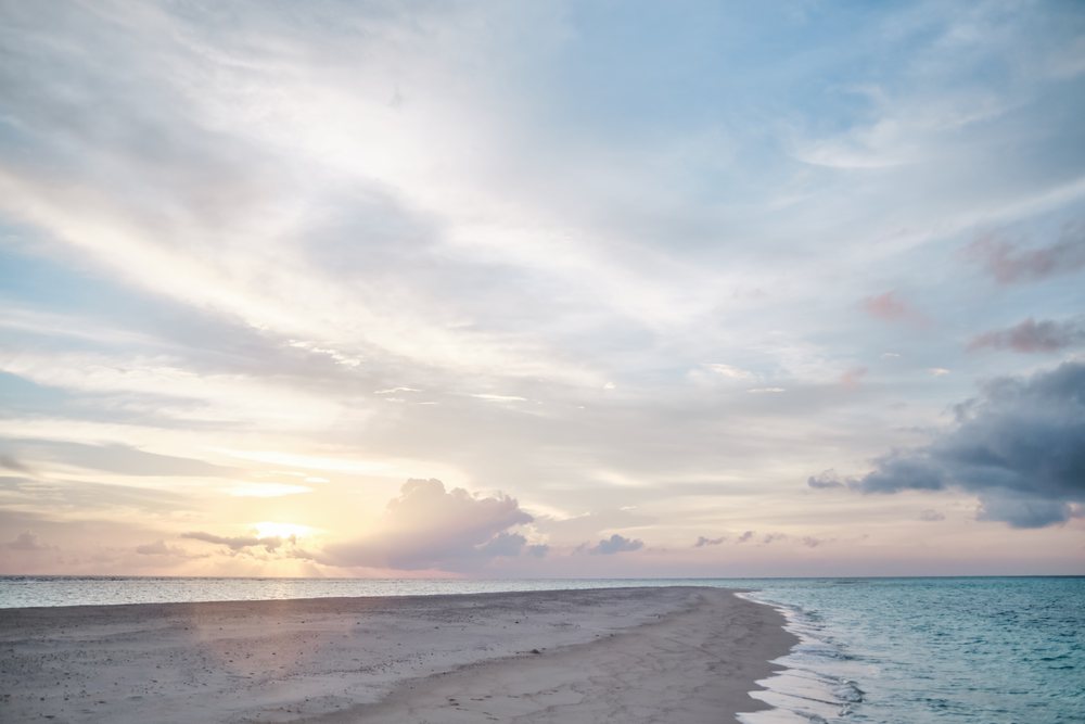 A tranquil sandbar stretches into the ocean at sunset in the Maldives