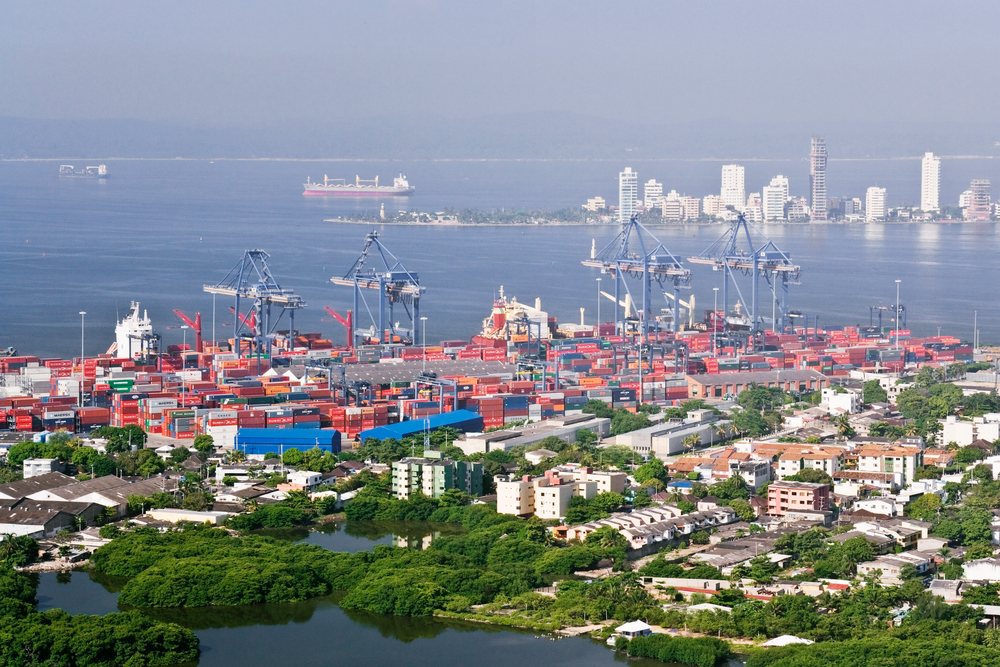 View of Port Cartagena container terminal with cranes, ships, and city buildings, Colombia.