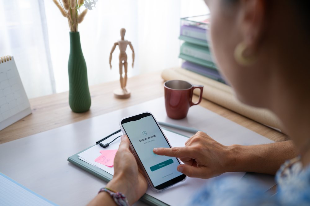 Person using a phone to verify identity with secure access at a home desk with office supplies, telecommuting, Spain.
