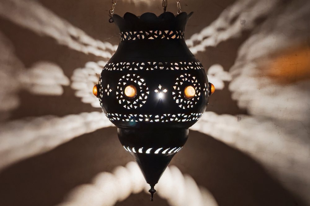 Metal Moroccan Lamp hanging indoors, casting intricate light and shadow patterns on the wall, Lifestyle, Landscape, Culture, Marrakech, Marrakesh-Safi Region, Morocco.