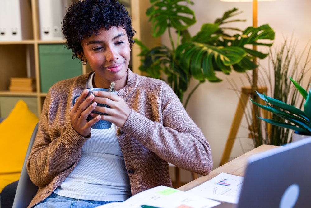 Woman holding a mug and smiling while sitting at a desk in a home office environment with plants, Spain.