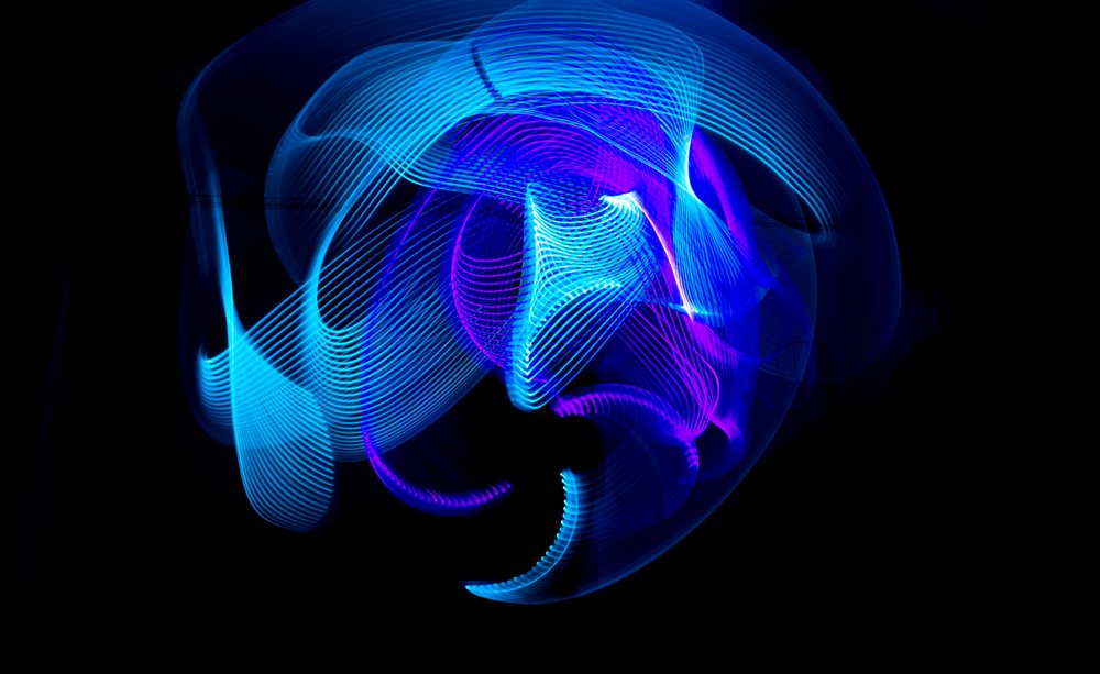 LED light painting shows blue and purple glowing abstract patterns with curved light trails on a dark background.