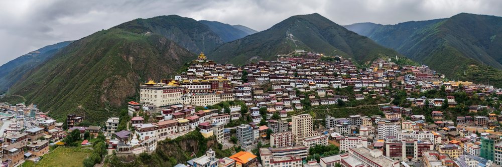 Baiyu Monastery perched on a hillside among Tibetan buildings with mountainous green landscape, China, Sichuan Province, People's Republic of China.