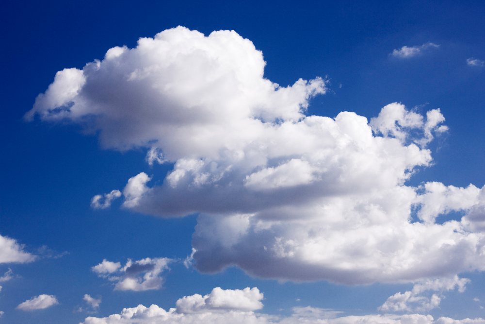 Fluffy white cumulus clouds float in a clear blue sky on a bright day outdoors.