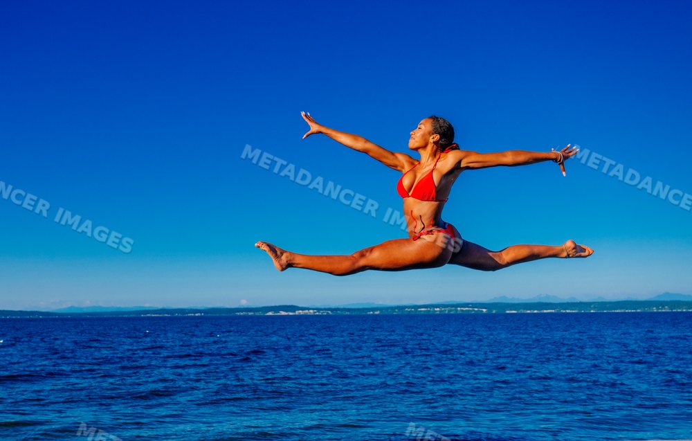 Woman in red swimsuit jumping in a split leap over the ocean