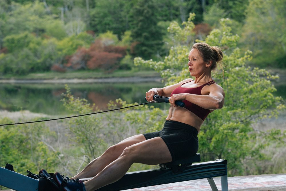 Woman exercising on a rowing machine outdoors near a lake, USA.