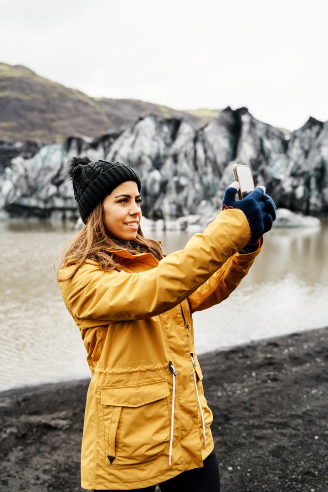A white woman takes a photo at a glacier lake