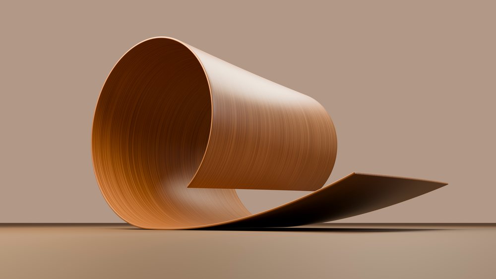 Curled plywood sheet with smooth wood grain texture on a brown wood veneer surface in a studio setting.