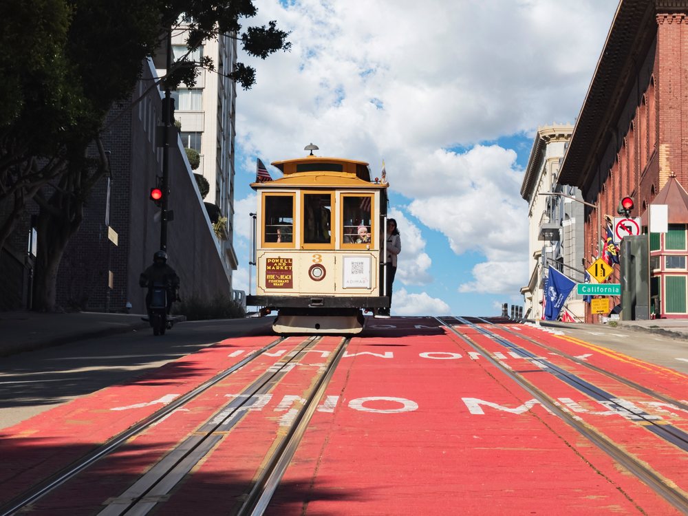 San Francisco Cable Car traveling uphill on California Street with passengers and city surroundings on a clear day, landscape, cityscape, city life, USA.