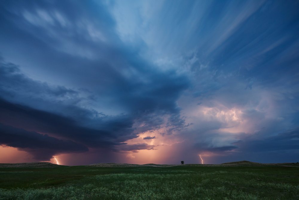 Lightning strikes from storm clouds over a green grassy field in a rural open landscape, Storm Chasing, Weather, Environmental Issues, Dunning, Nebraska, USA.