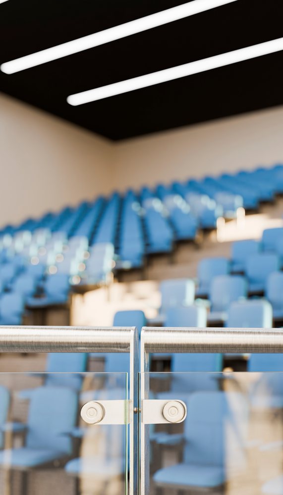 Blue stadium seats arranged in rows behind a glass barrier with brushed steel handrails in an empty indoor venue.