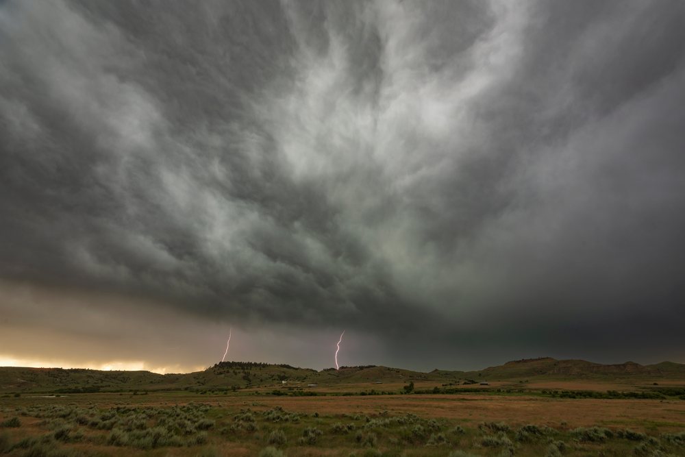 Lightning strikes beneath dark Storm Clouds over grassy hills in Tornado Alley, Gillette, Wyoming, USA.
