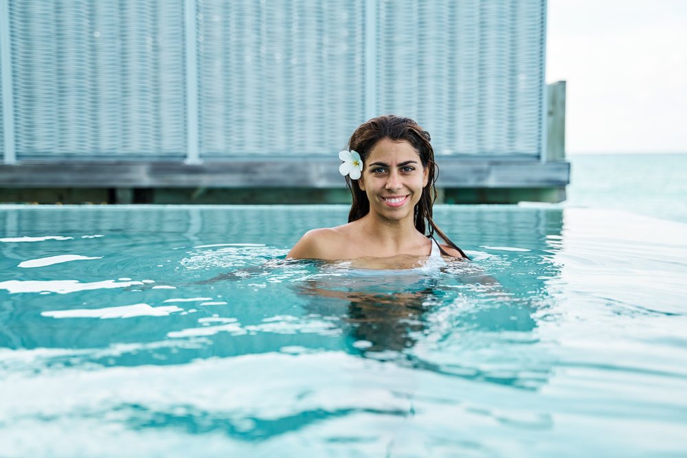 A smiling white woman swims in an infinity pool at a resort