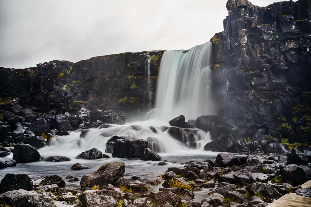Water cascades over rocks forming a waterfall in a rocky landscape on a cloudy day, Iceland.