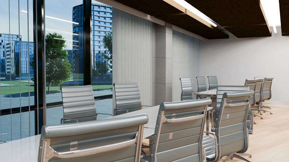 Bright conference room with white table and modern chairs next to large floor-to-ceiling windows showing urban buildings outside.