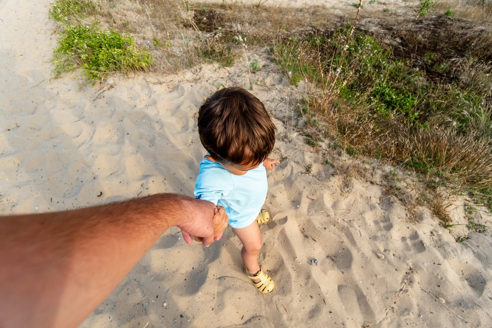 Child holding an adult's hand walking on sand outdoors in Spain during summer, kids.