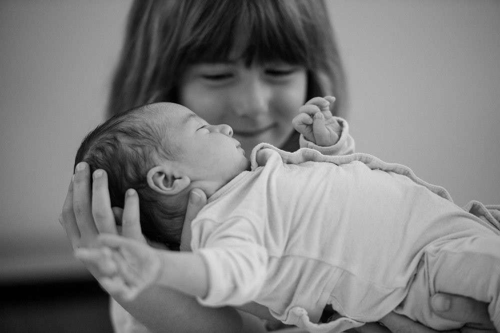 Sleeping newborn gently held by a smiling child in a tender indoor moment, USA.