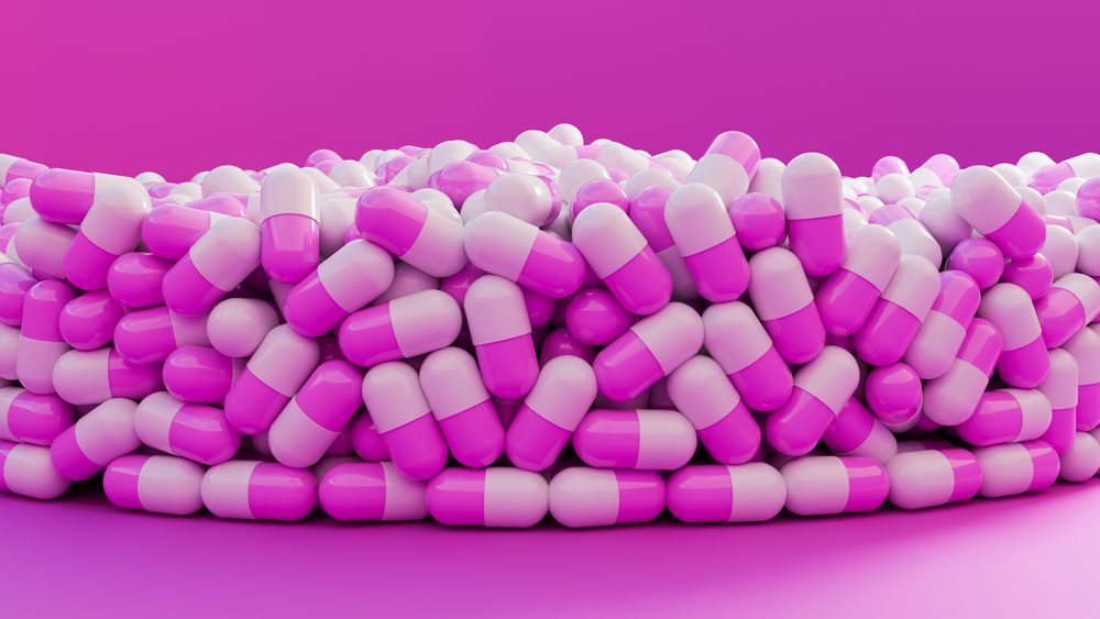 Pile of pink and white medicine capsules arranged on a pink background.