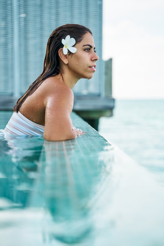 A white woman relaxes in a swimming pool overlooking the ocean