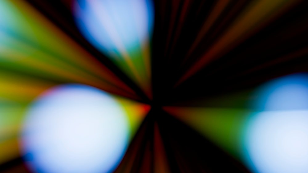 Abstract colorful and blurred pattern featuring radiating beams of light and glowing vibrant circles on a dark background.