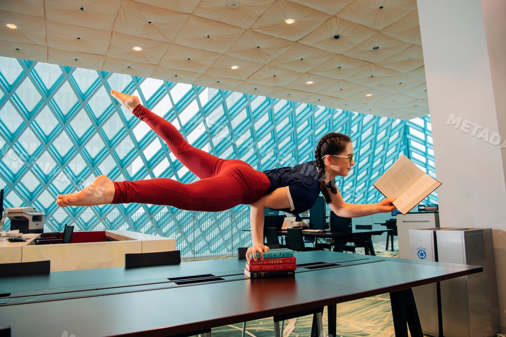 A woman performs a yoga handstand while reading a book
