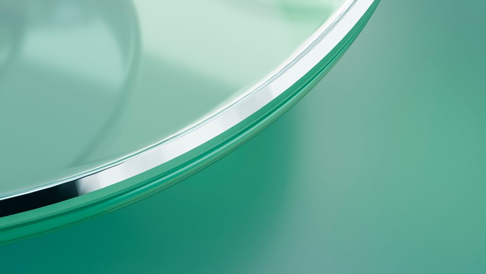 Close-up of a transparent glass dish with reflective edges on a green background.
