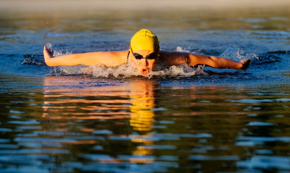 Swimmer performing butterfly stroke in open water wearing a swim cap and goggles, USA.