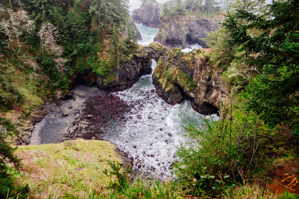 Natural rock bridge spans a narrow ocean inlet with waves and sea foam, Boardman State Scenic Corridor, Oregon, USA.