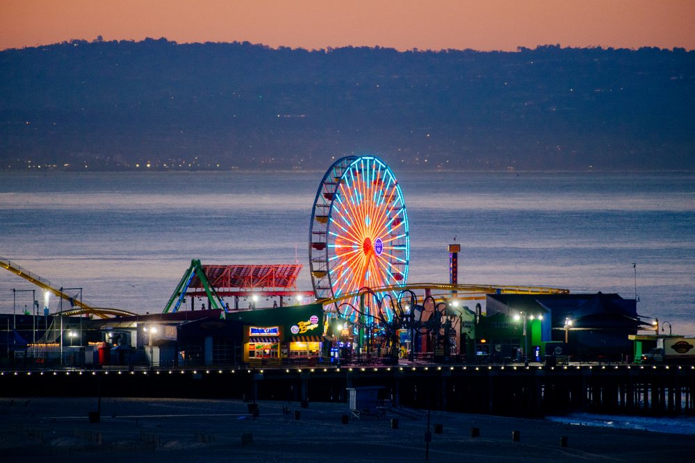 Santa Monica Pier showing ferris wheel illuminated at sunset with ocean and beach views in lifornia, CA, USA.