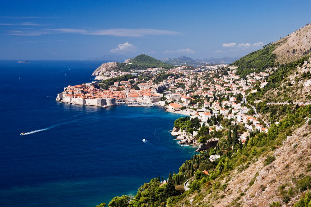 The Old City of Dubrovnik with medieval fortress walls and boats along the Dalmatian coast on the blue Mediterranean Sea.