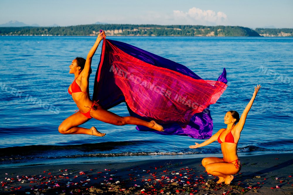 Two women performing yoga partner acrobatics on a beach with ocean