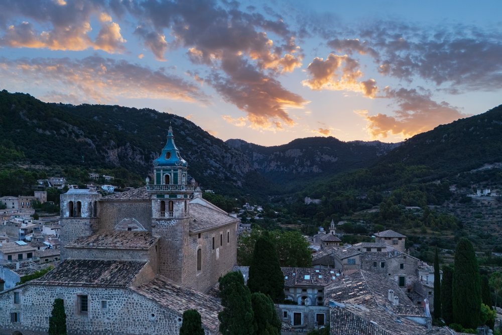 Sunrise over Valdemossa village with historic church tower and surrounding mountain landscape, Mallorca, Spain.